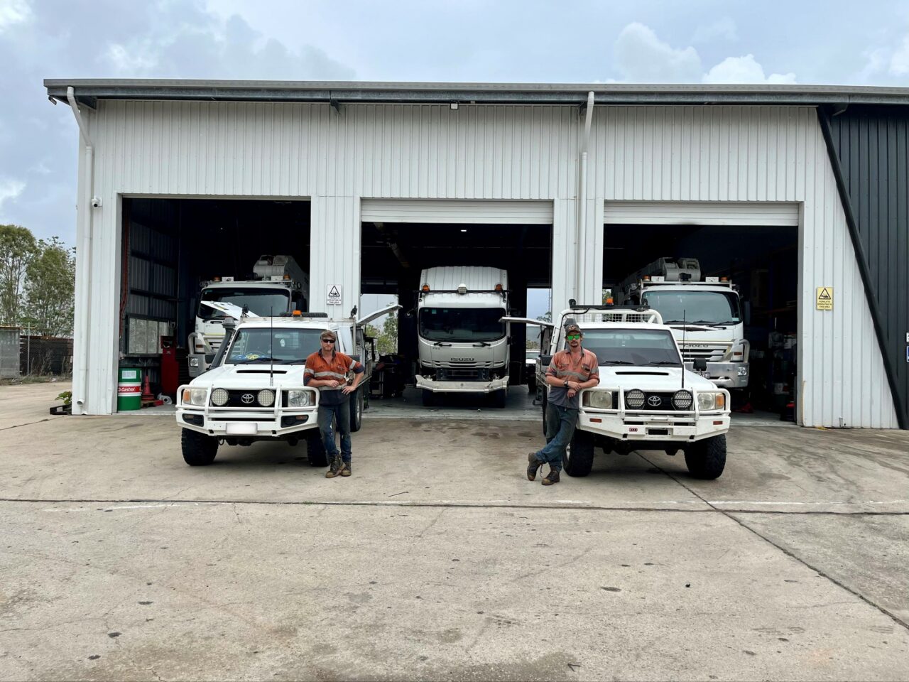 BDS mechanical repairs mechanics standing in front of the townsville workshop with the ergon energy trucks